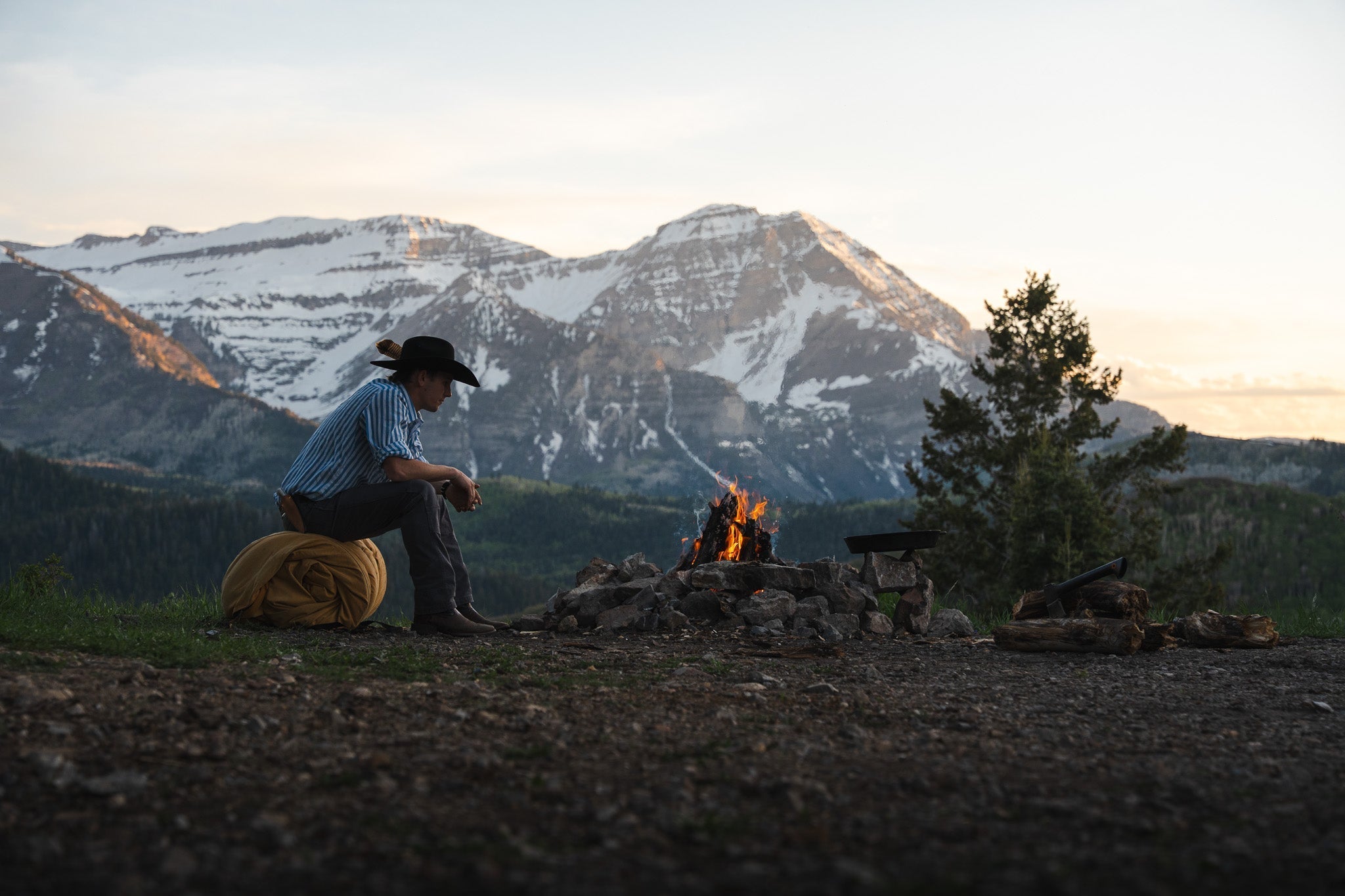 Man using a cowboy bedroll near a campfire in the mountains, real-world canvas camping gear in action