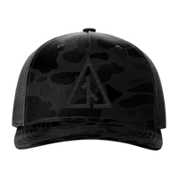 Front view of the Canvas Cutter Darkwater Hat featuring a black camouflage cap with a logo on a blackout five panel trucker design