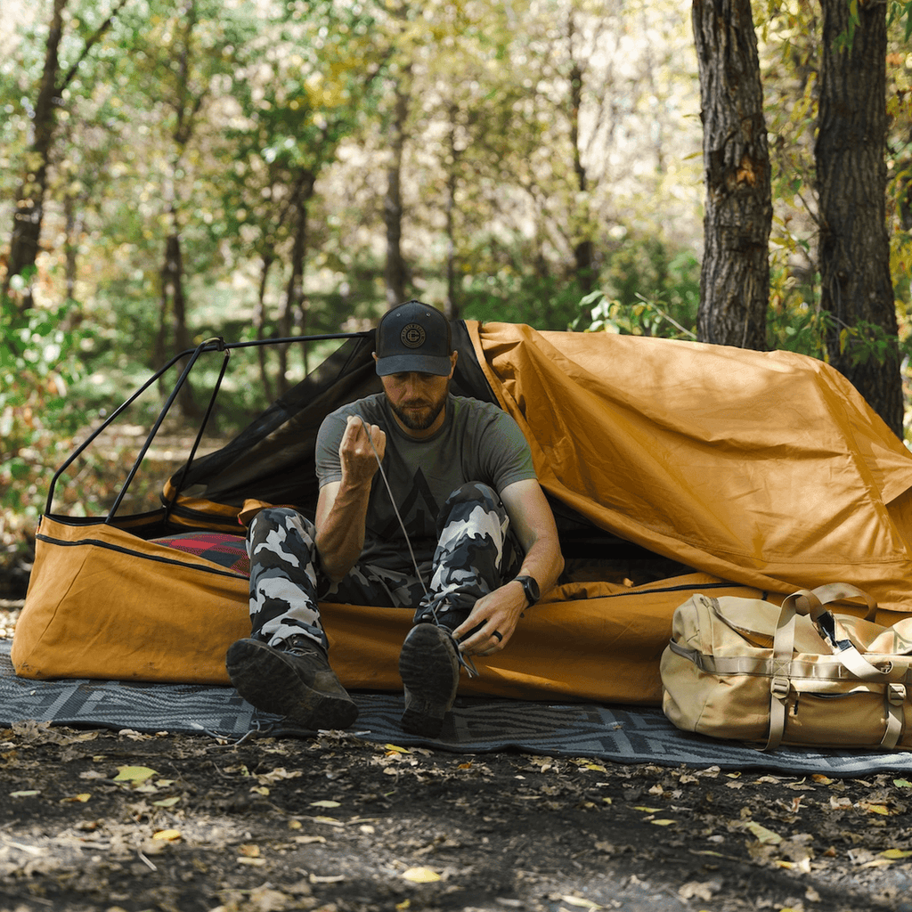 Person sitting inside the Dominator 3.0 bedroll with the canvas unzipped, showing interior space and comfort
